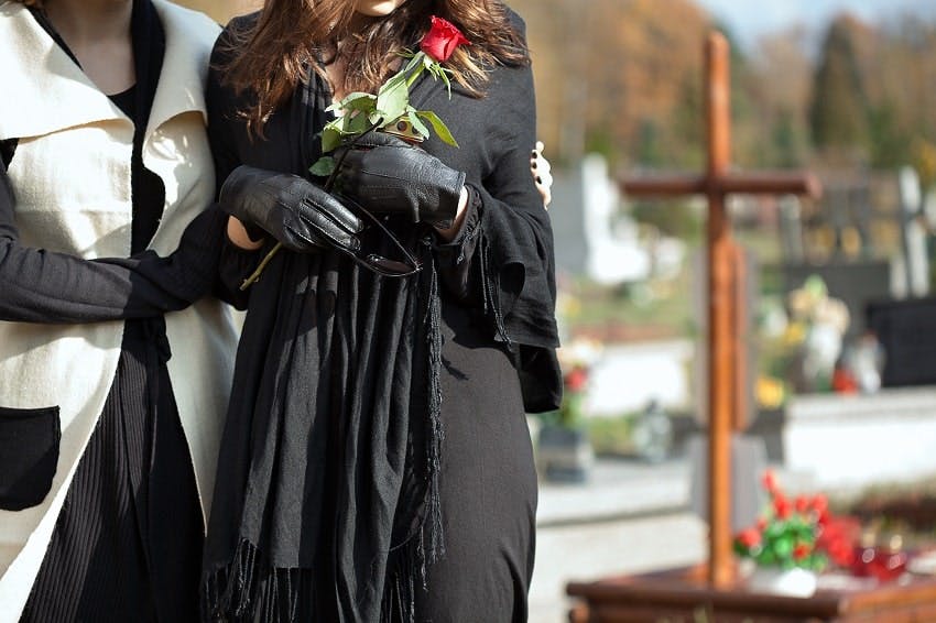 une femme soutenant une autre femme habillée en noir et portant une rose rouge dans un cimetière