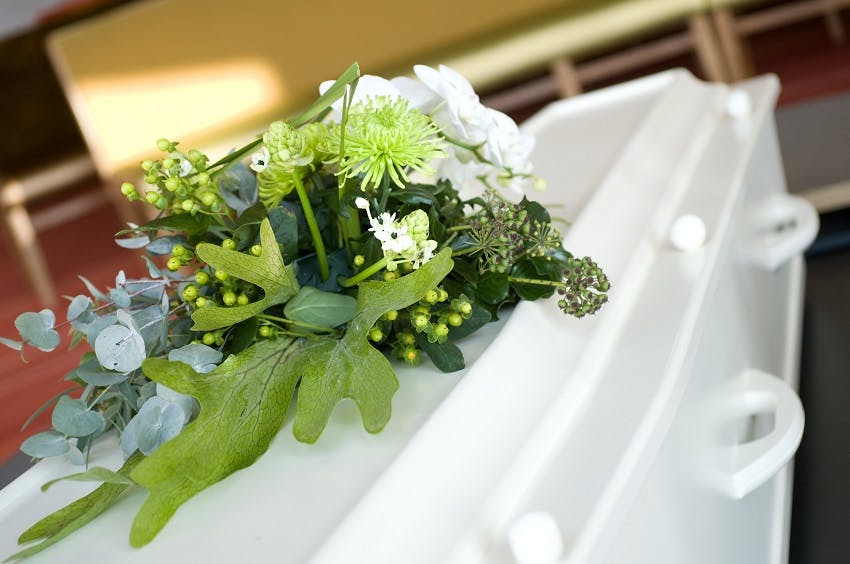 cercueil blanc avec coussin de fleurs blanches et de feuilles vertes