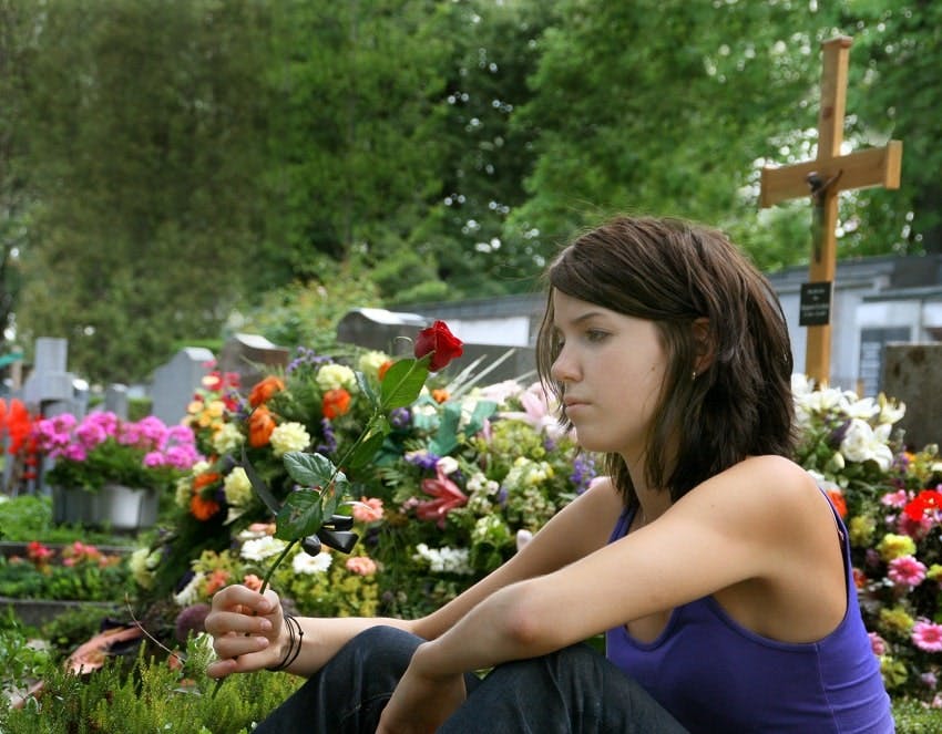 jeune fille assise à côté d'une tombe et tenant une rose rouge