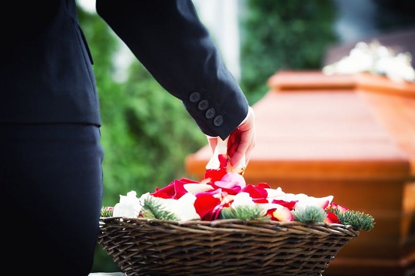 personne prenant des pétales de rose d'un panier à côté d'un cercueil 