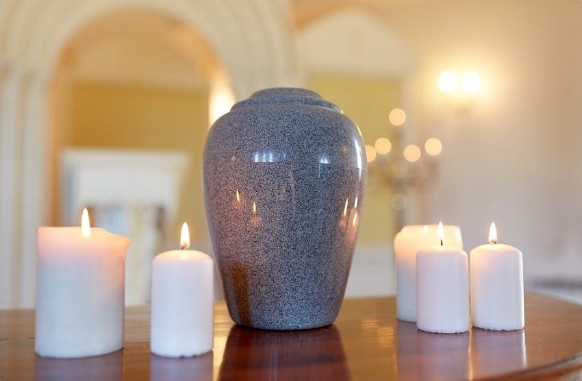 urne funéraire grise posée au milieu de bougies blanches allumées