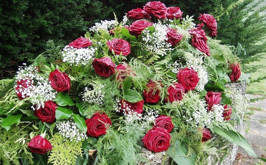 composition florale funéraire avec des roses rouges, du feuillage et des petites fleurs blanches