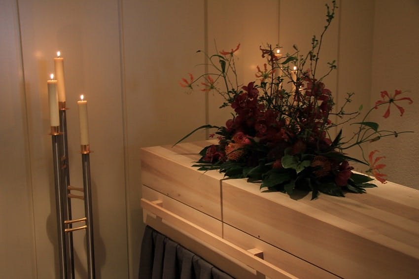 cercueil en bois dans une chambre funéraire avec fleurs et bougies allumées à côté
