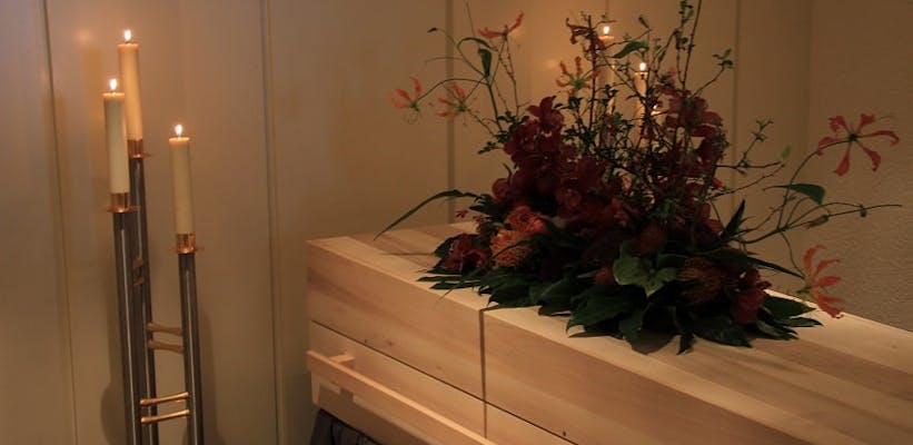 cercueil en bois dans une chambre funéraire avec fleurs et bougies allumées à côté