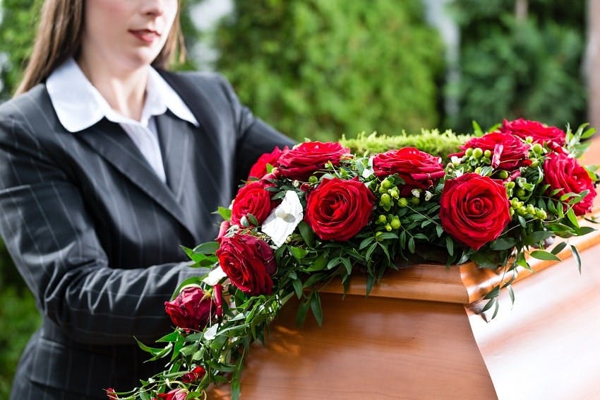 femme se tenant à côté d'un cercueil sur lequel est posé un coussin de fleurs de deuil avec des roses rouges