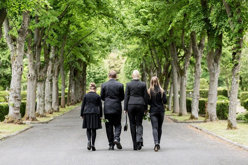 deux adultes et deux enfants habillés en noir dans l'allée d'un cimetière