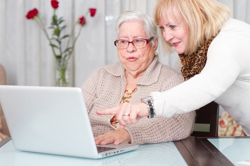 femme montrant l'écran d'un ordinateur à une personne plus âgée 