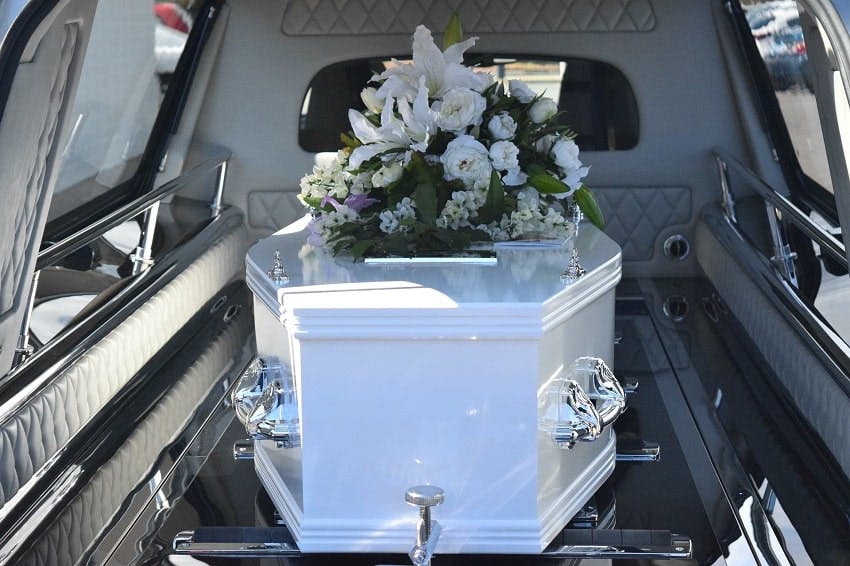 cercueil blanc dans un corbillard avec un coussin de fleurs blanches d'obsèques