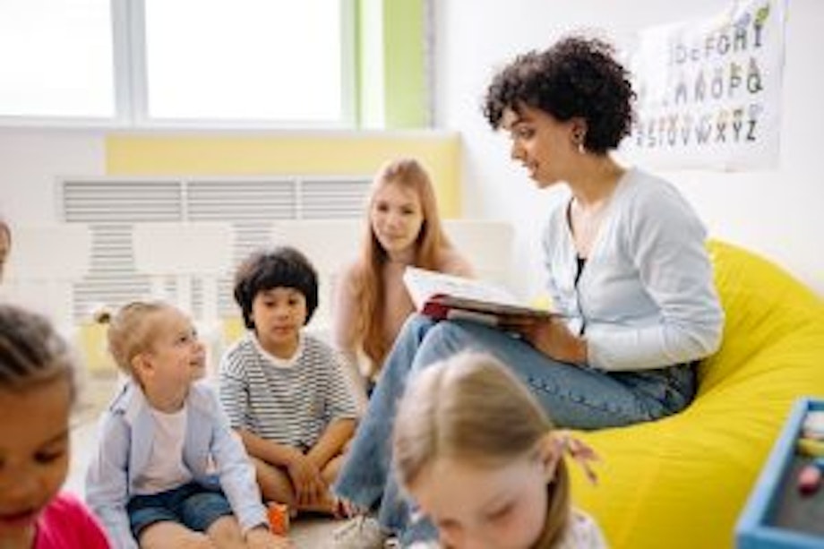 Eine junge Lehrerin sitzt auf einem gelben Sitzsack und liest Kindern vor