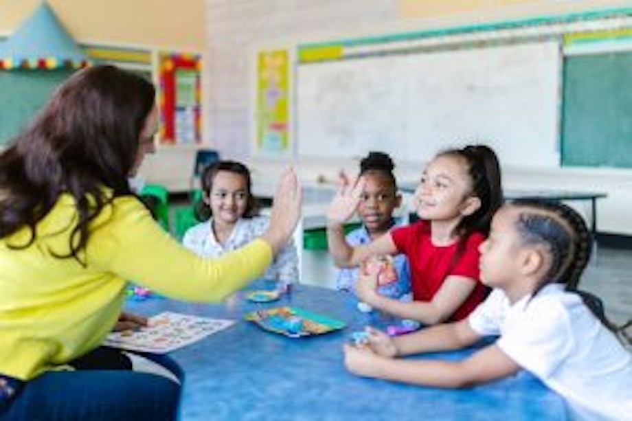 Eine Lehrerin sitzt mit ihren Schülerinnen im Kreis, die Mädchen lachen