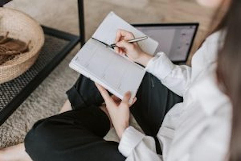 Eine junge Frau sitzt auf dem Sofa und hält einen Terminkalender und einen Stift in der Hand