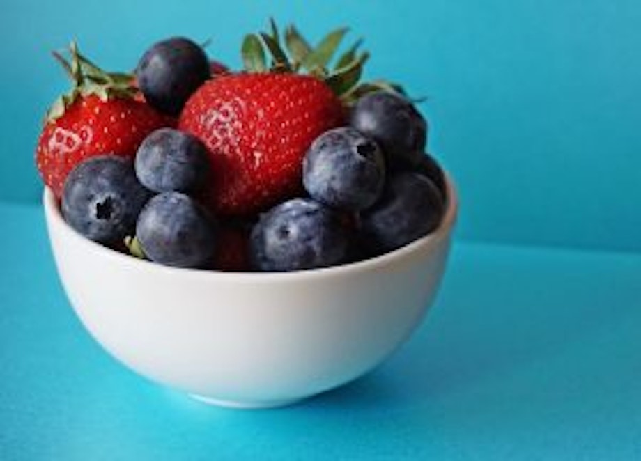 Eine weiße Obstschale mit Blaubeeren und Erdbeeren auf einem blauen Untergrund