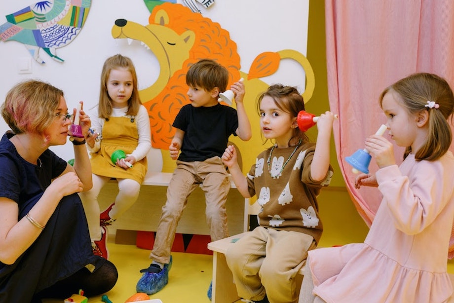 Schüler und Schülerinnen spielen mit farbenfrohen Glocken, neben ihnen kniet eine Lehrerin