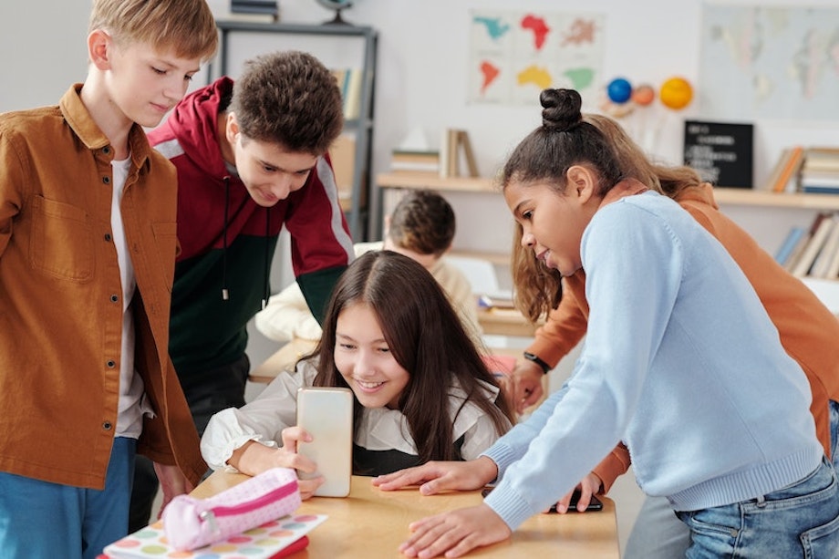 Schülerinnen und Schüler stehen an einem Tisch im Klassenzimmer und sehen sich ein Video auf einem Smartphone an