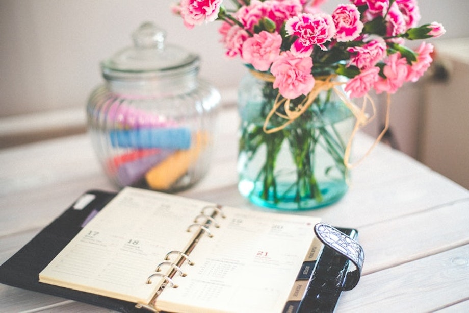 Ein Kalender liegt auf einem Holztisch, dahinter steht eine Blumenvase. Einen Korrigierkalender zu führen, ist sehr hilfreich, wenn du deinen Korrekturprozess besser organisieren möchtest. Wir geben dir praktische Tipps dafür.