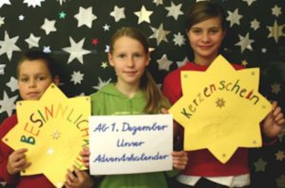 Drei Kinder stehen vor einer Sternenwand und präsentieren einen Adventskalender. Die Schüler und Schülerinnen können sich Rezepte, Geschichten, Bastelideen überlegen und so einen Wissenskarten-Adventskalender gestalten.