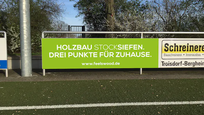 Grün/Weiße Sportplatzbande mit dem Claim "Drei Punkte für Zuhause" des Unternehmens Stocksiefen - Handwerk Marketing von der Meisterstück Agency aus Köln.