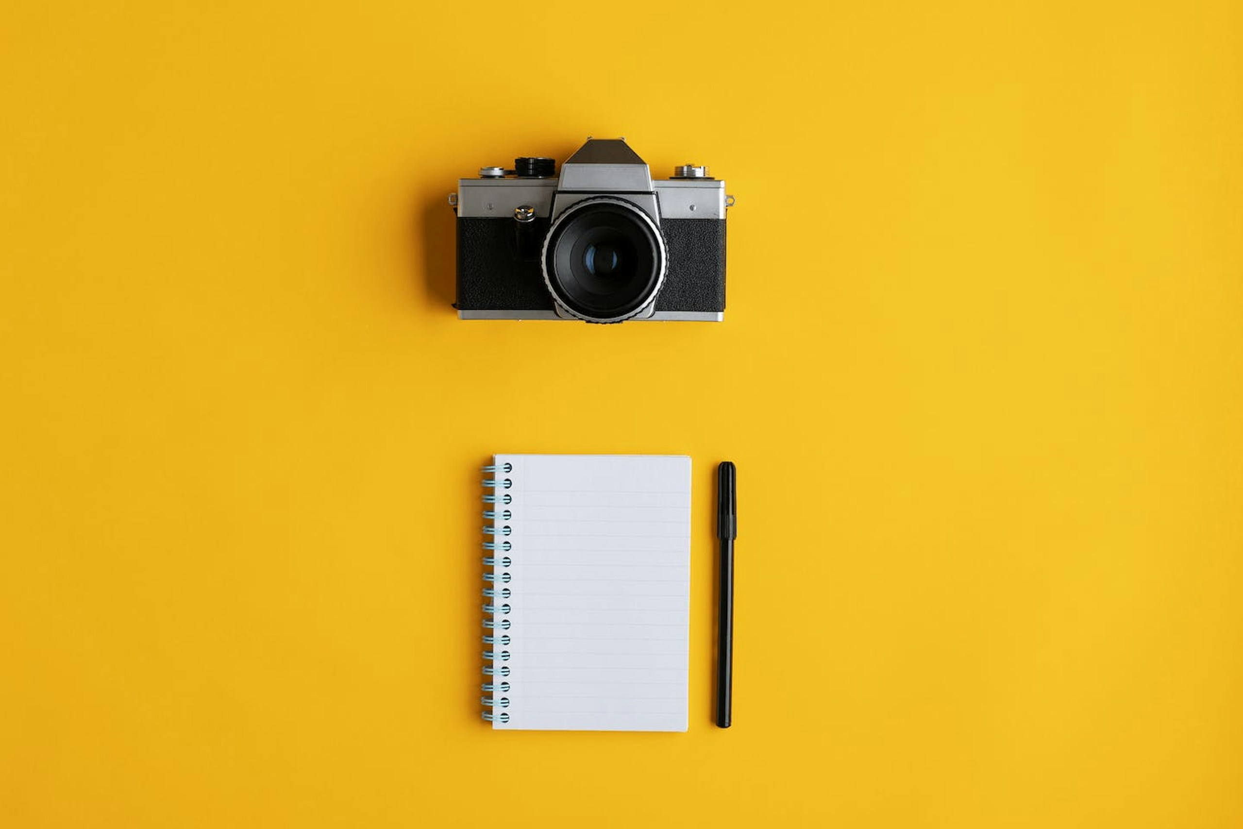 Eine Kamera, ein Schreibblock und ein Stift vor einem gelben Hintergrund