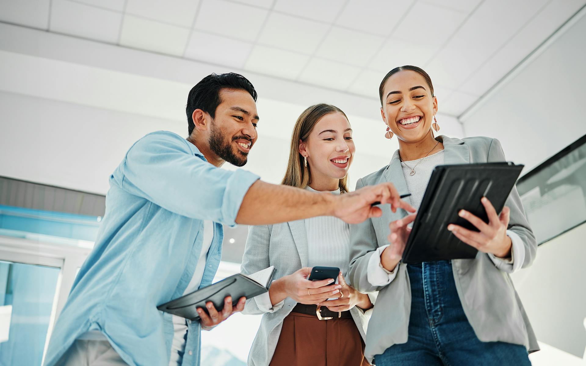 A group of happy social media marketers  in an office looking and pointing at a tablet.