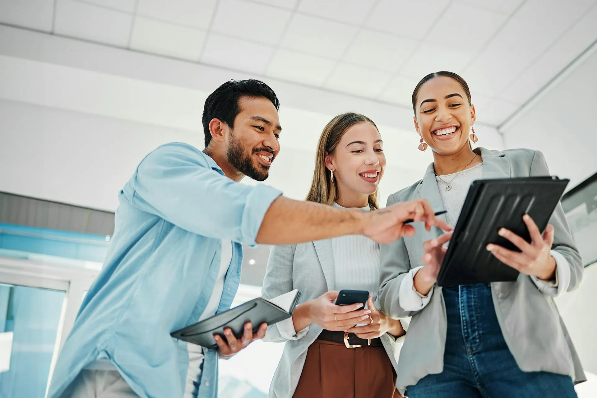 A group of happy social media marketers in an office looking and pointing at a tablet.