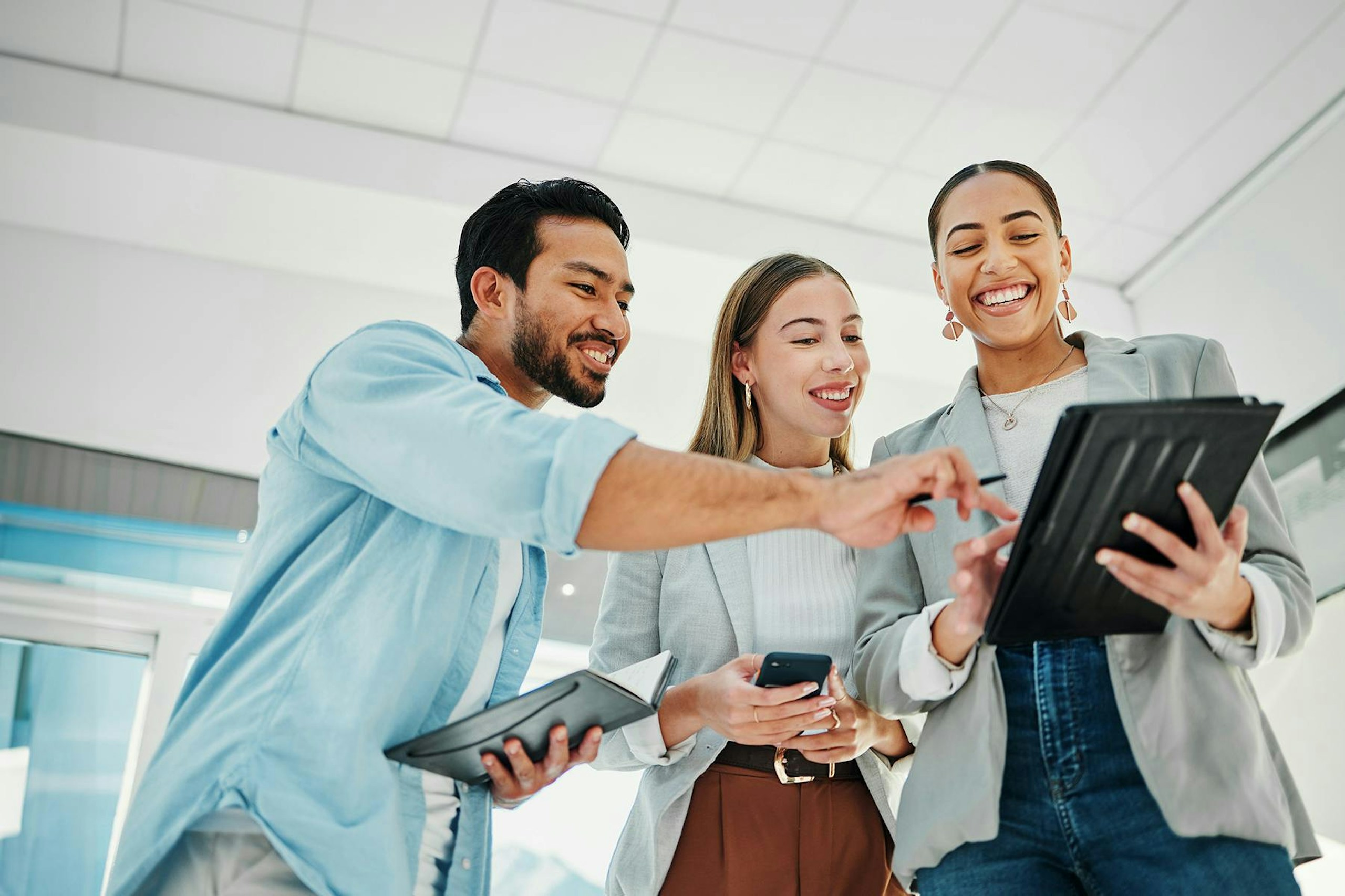 A group of happy social media marketers in an office looking and pointing at a tablet.