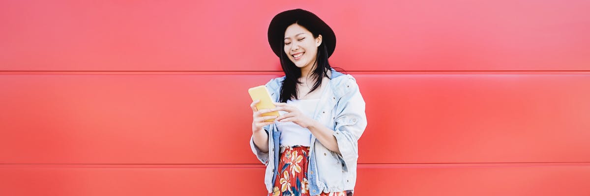 A woman standing against a bright red wall playing on her phone.