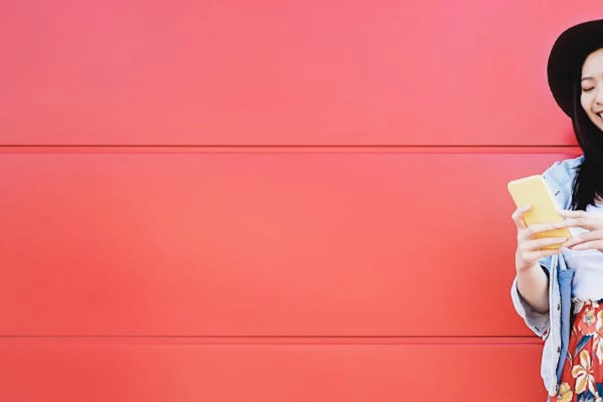 A woman standing against a bright red wall playing on her phone.
