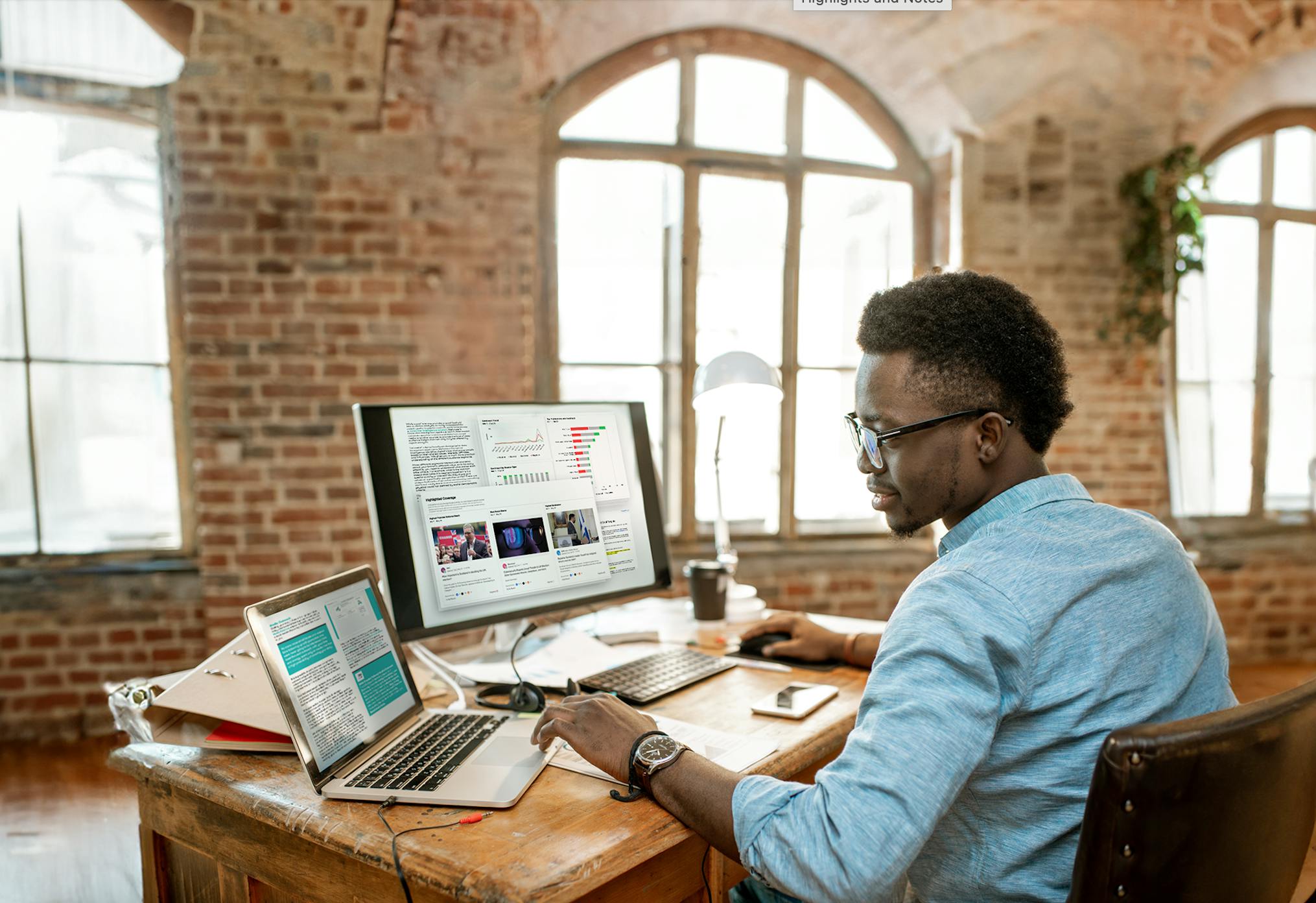 Image of a PR professional sitting at his desk in front of a large monitor and laptop. The computers show various charts and tools for PR professionals. PR Toolkit download