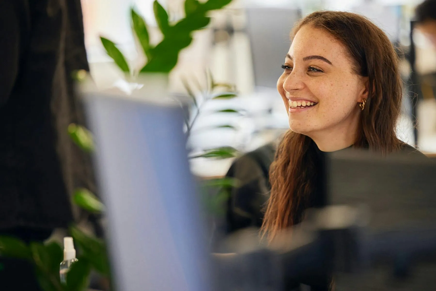 A redheaded person smiles in a busy office in this header image for Meltwater's customer story about CCGroup.