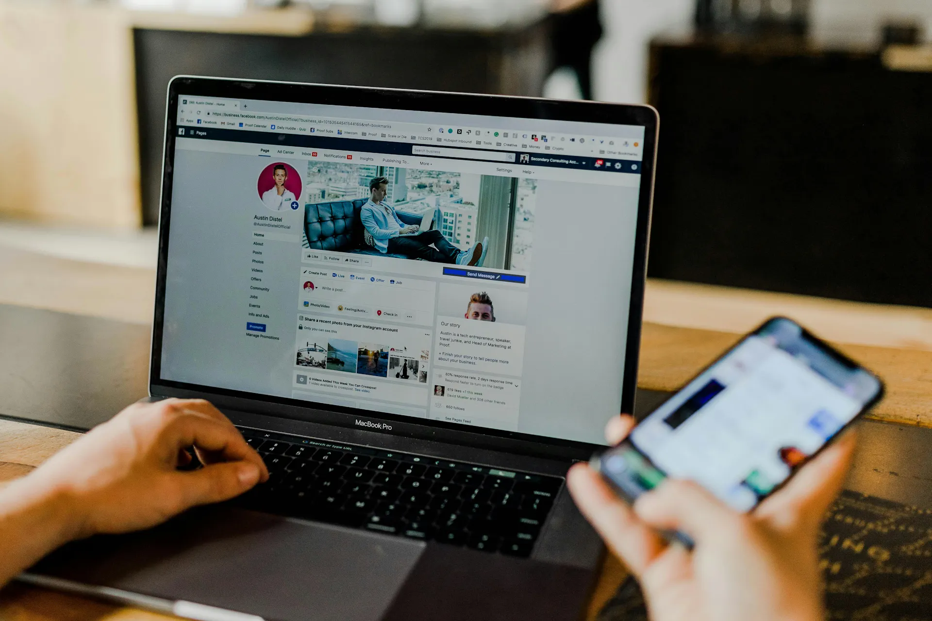 person holding an out of focus phone with facebook on the laptop screen