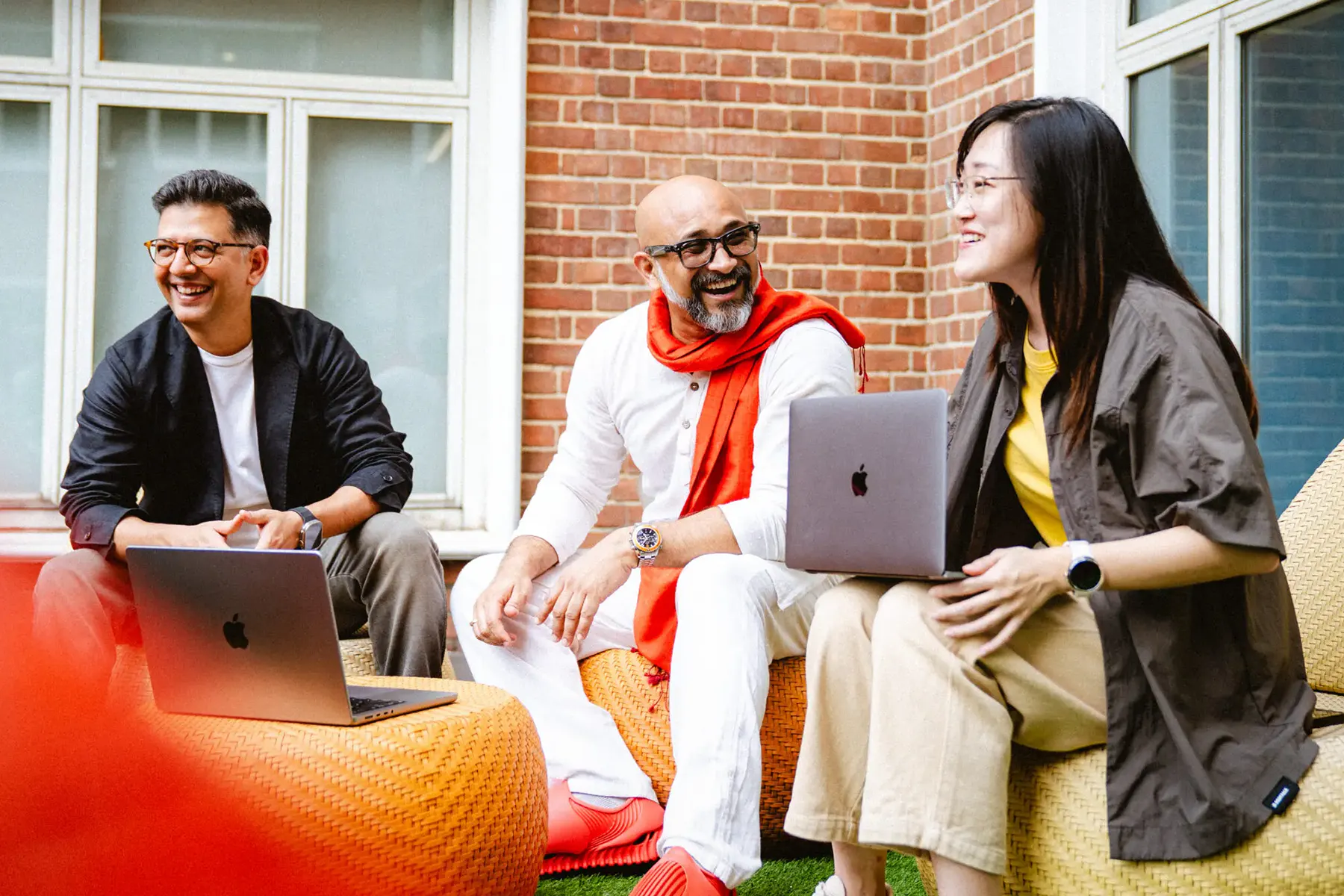 Three Golin Ketchum colleagues smiling and working together outdoors with laptops.