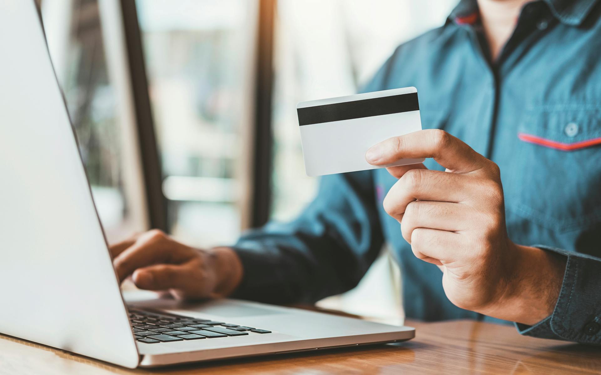 A person types at a laptop and holds a credit card in this image for Meltwater's Industry Snapshot: Banking and Financial Services
