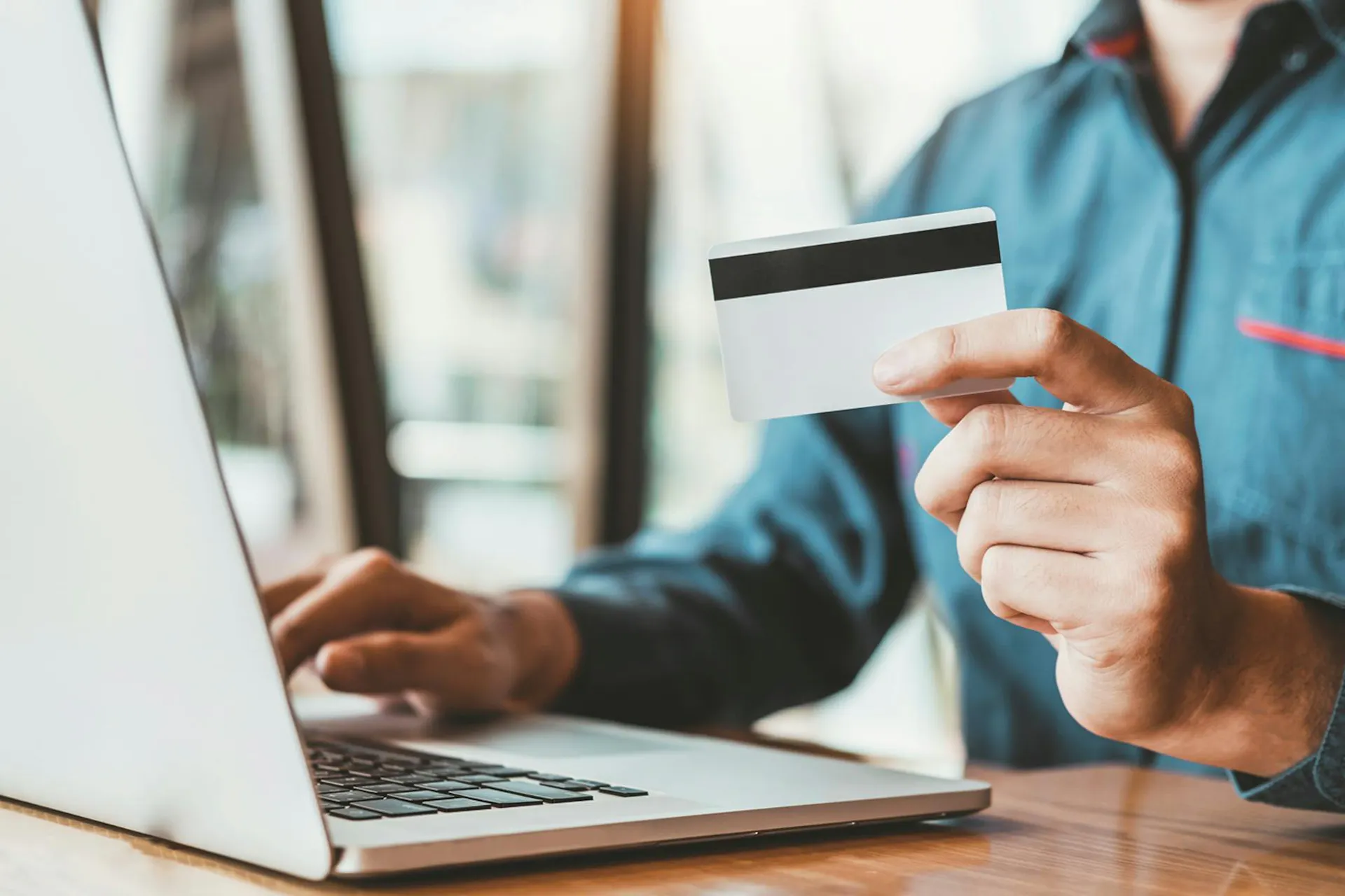 A person types at a laptop and holds a credit card in this image for Meltwater's Industry Snapshot: Banking and Financial Services