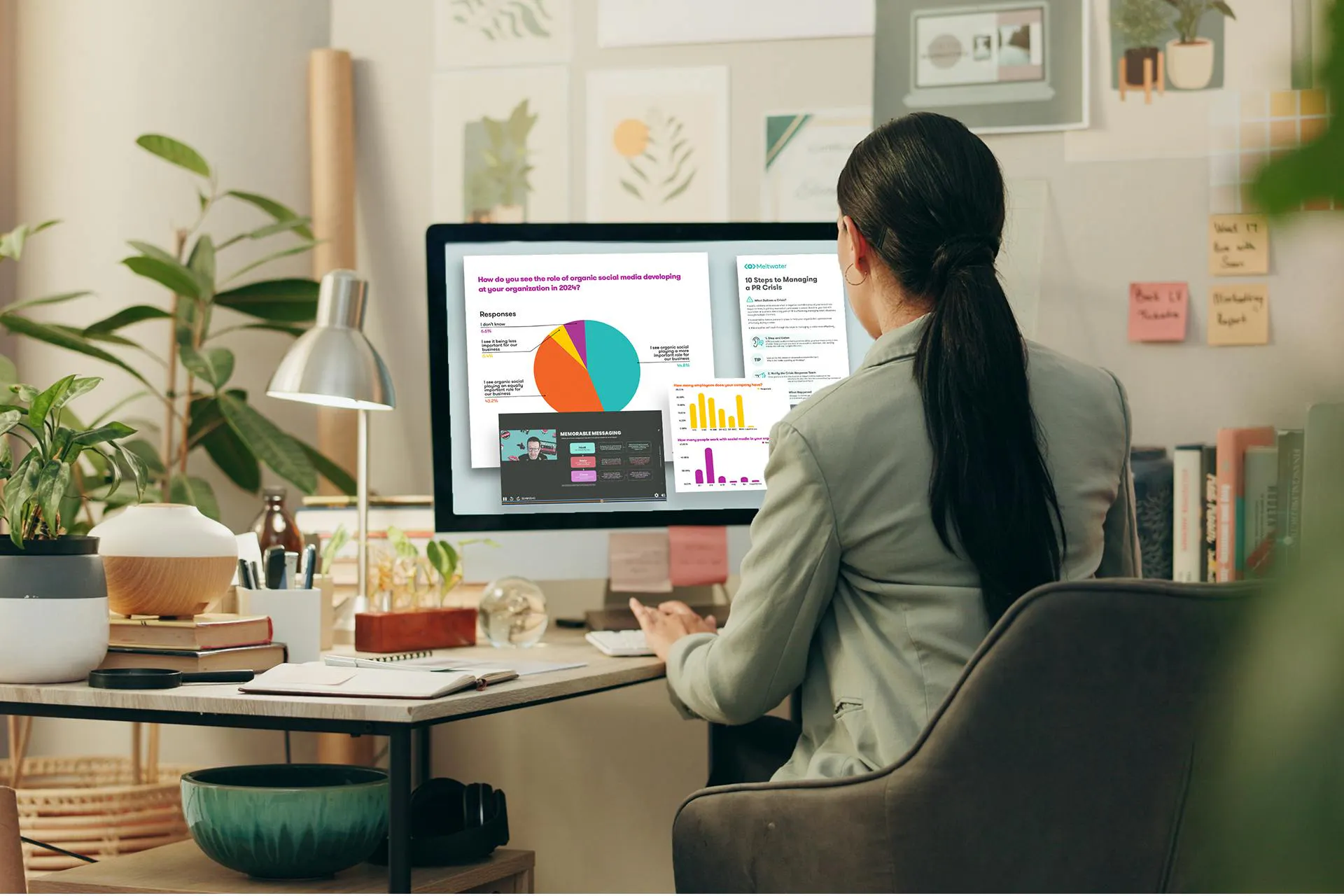Image of a social media manager sitting at her desk in front of a large desktop computer. The computer shows various charts and resources for social media managers. Social Media Toolkit download