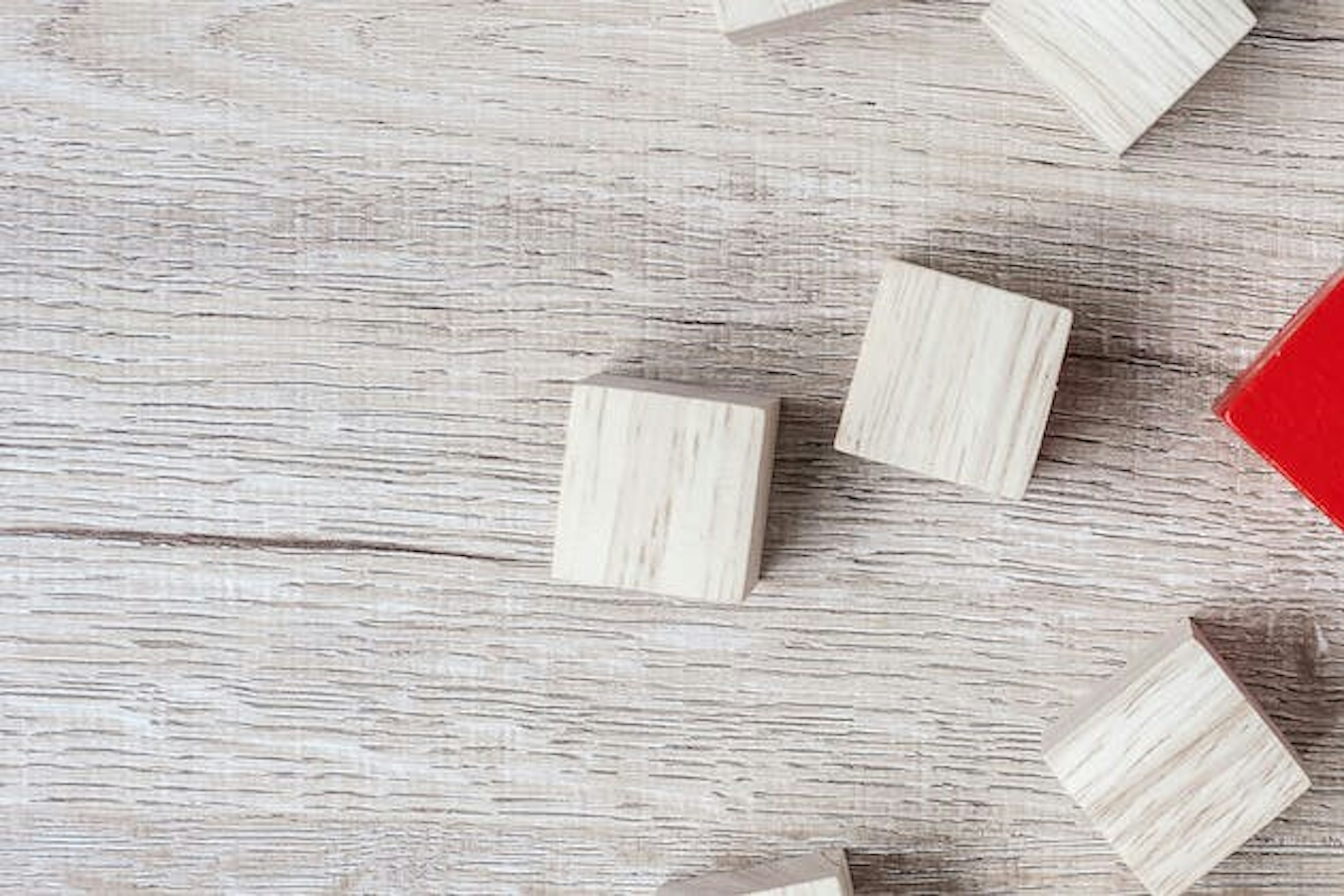Man sieht einen weiß gestrichenen Holztisch, auf dem viele weiße Holzwürfel zu sehen sind. In der Mitte sticht ein roter Würfel hervor. Dieses Bild ist das Titelbild unseres Beitrags zur Erarbeitung eines USPs / Alleinstellungsmerkmals.
