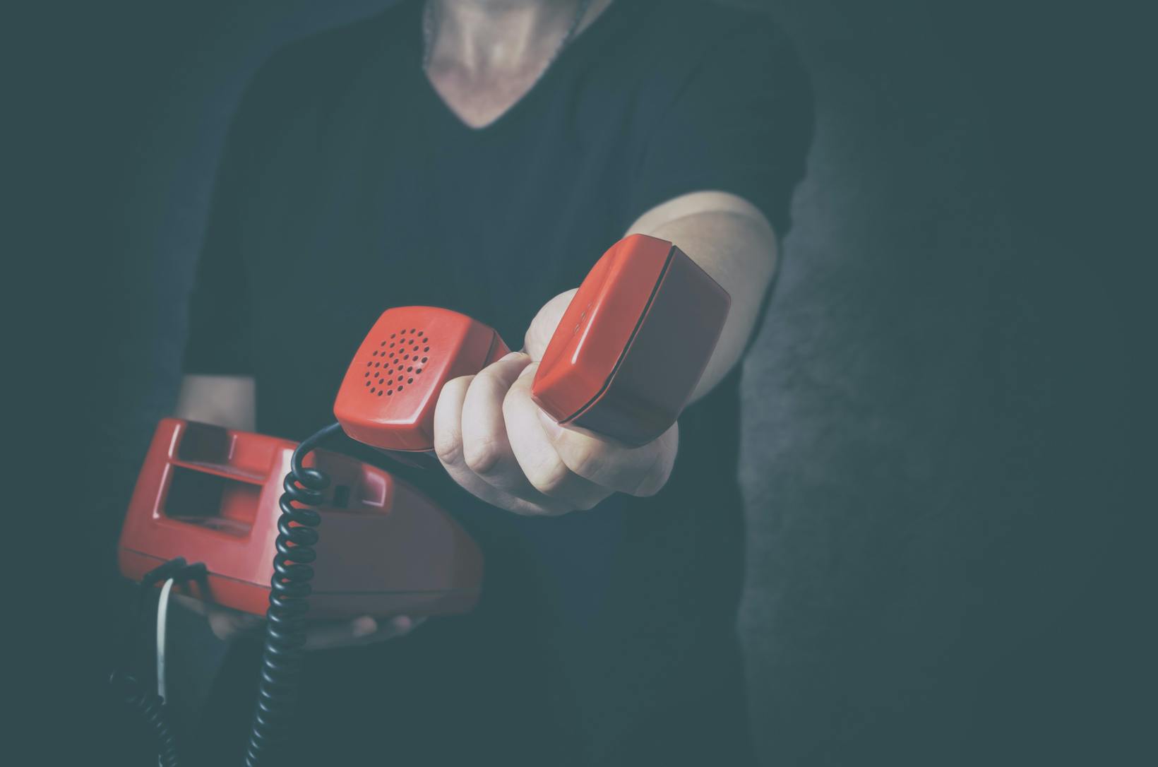 Mann hält rotes Schnurtelefon und hält Hörer in die Kamera