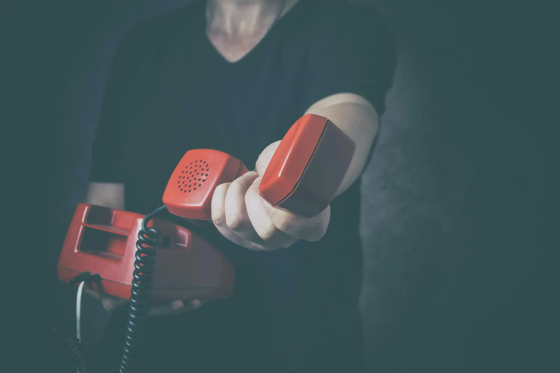 Mann hält rotes Schnurtelefon und hält Hörer in die Kamera