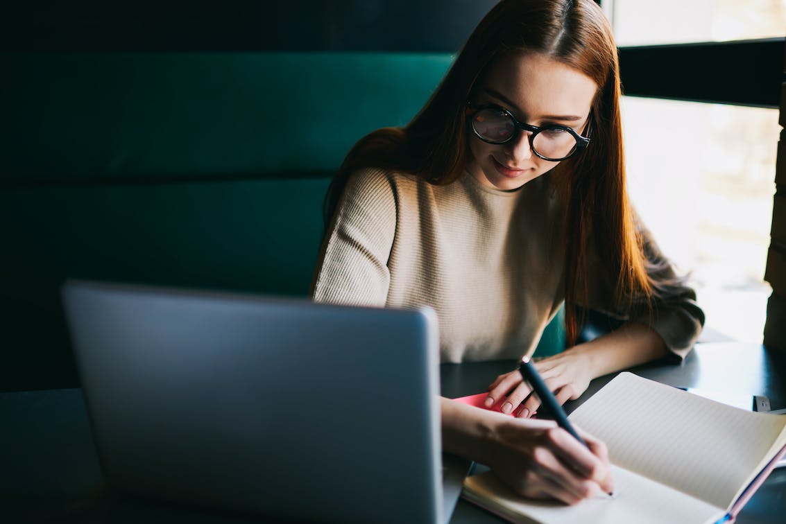 Junge Frau mit Brille arbeitet an ihrem Laptop und macht Notizen