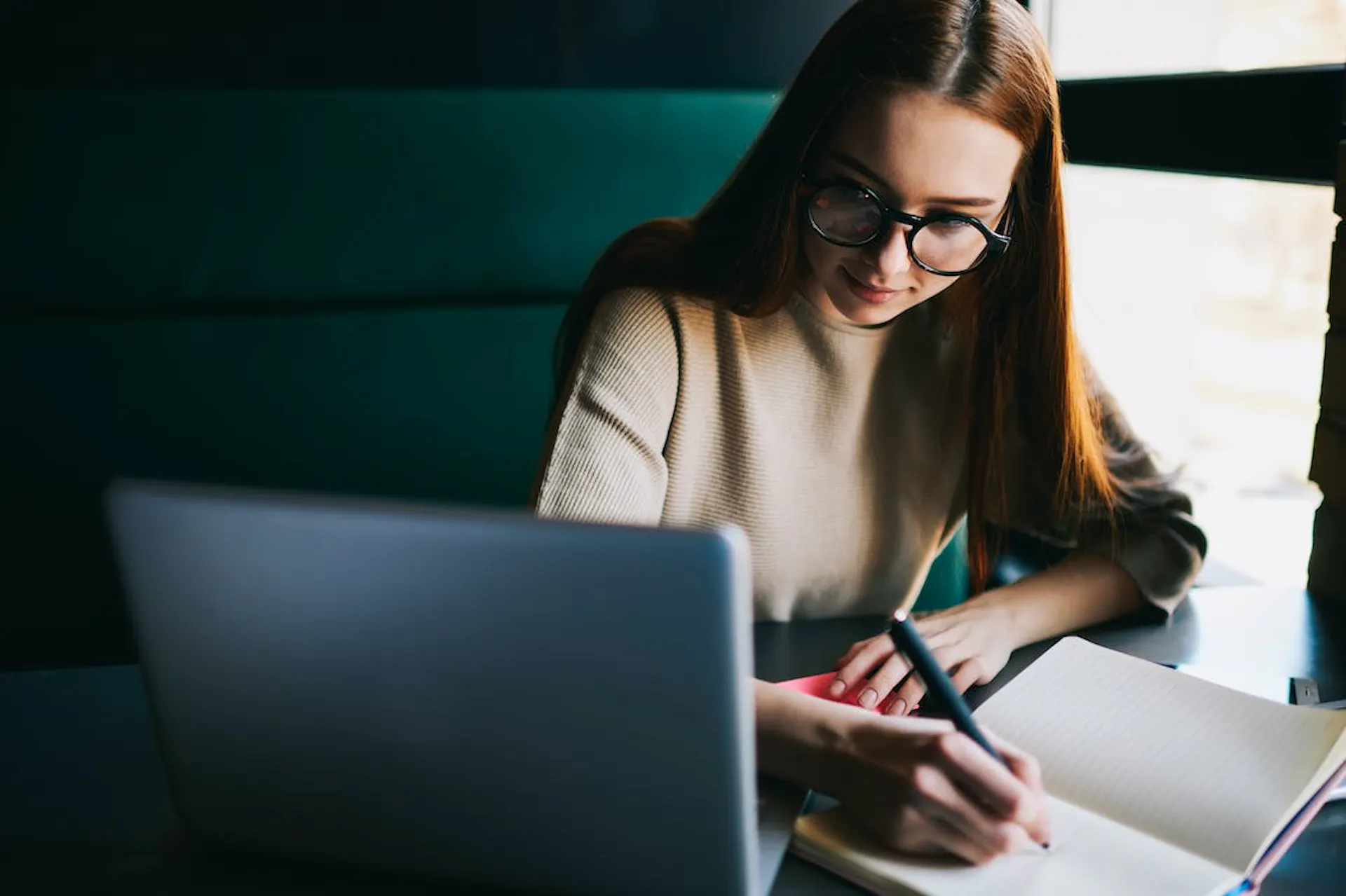 Junge Frau mit Brille arbeitet an ihrem Laptop und macht Notizen