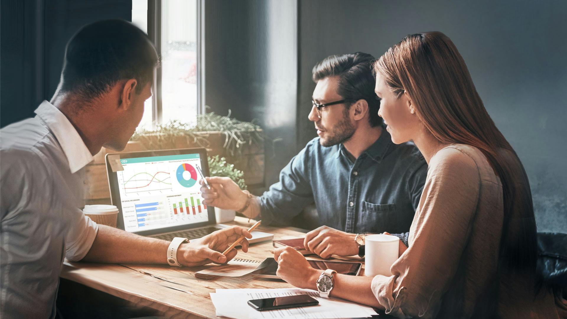 Photo of a team working on a laptop discussing Meltwater Media Intelligence dashboards