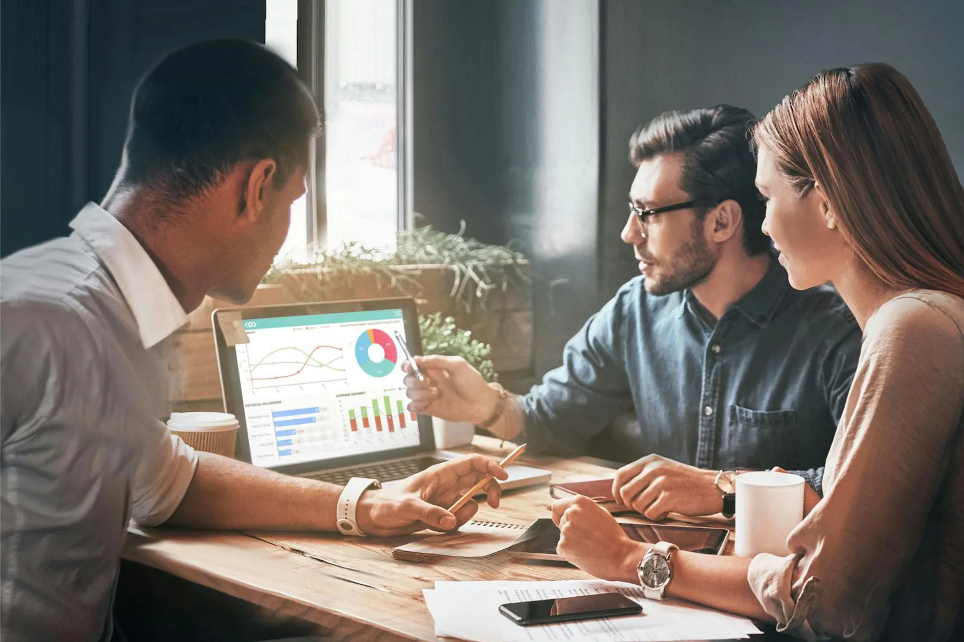 Photo of a team working on a laptop discussing Meltwater Media Intelligence dashboards