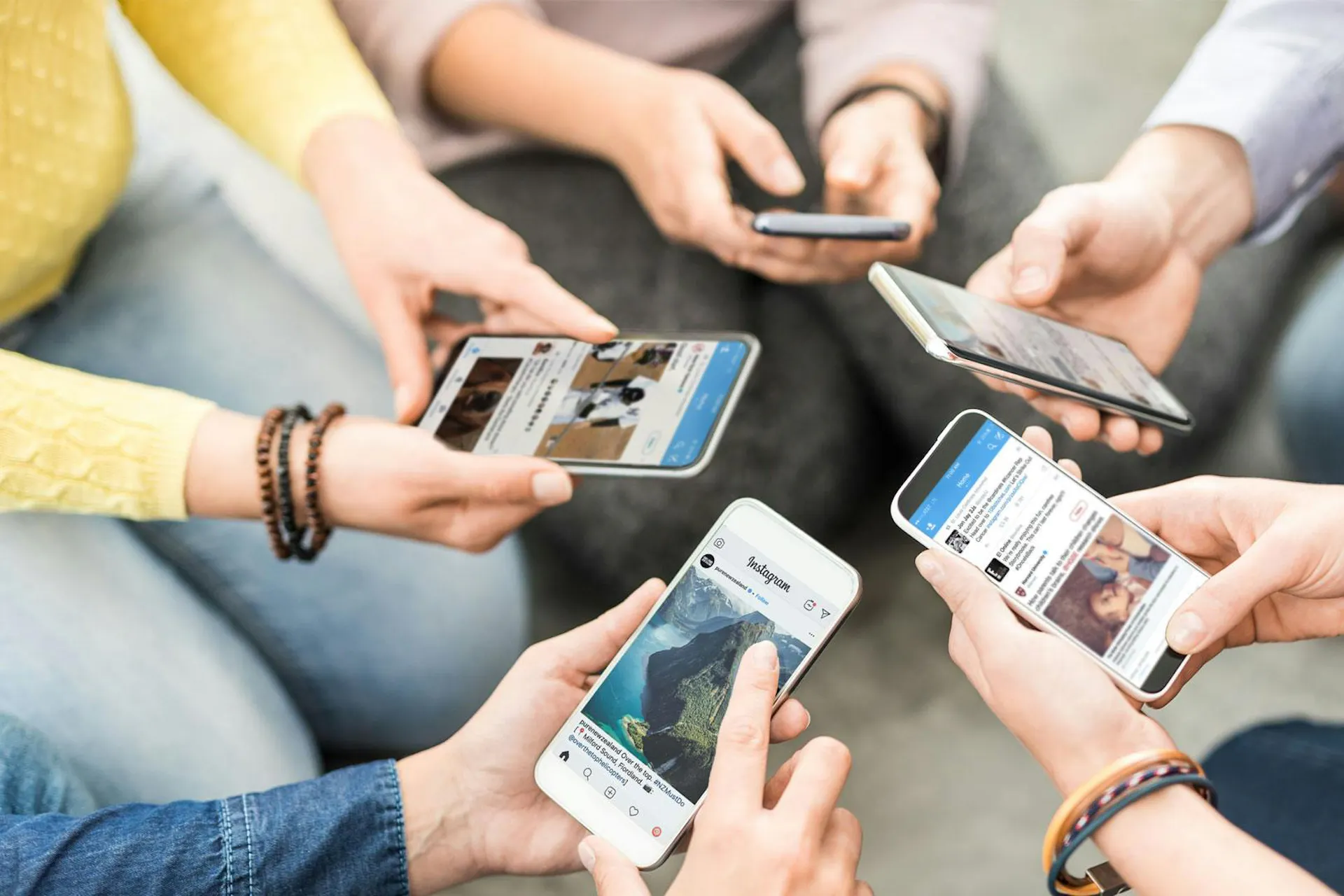 Photo of people sitting in a circle holding their smartphones into the middle