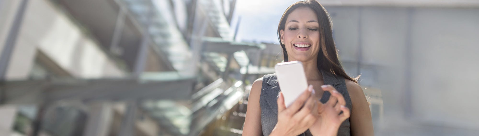 woman looking down on her phone with a smile on her face for social media phone use