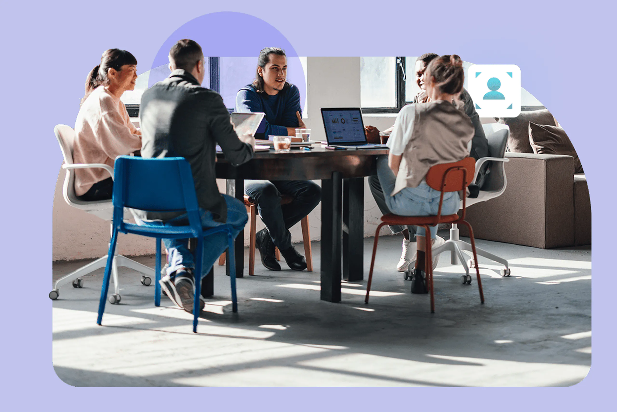 A photo of a group of professionals seated around a conference table collaborating in a modern office with laptops and natural light
