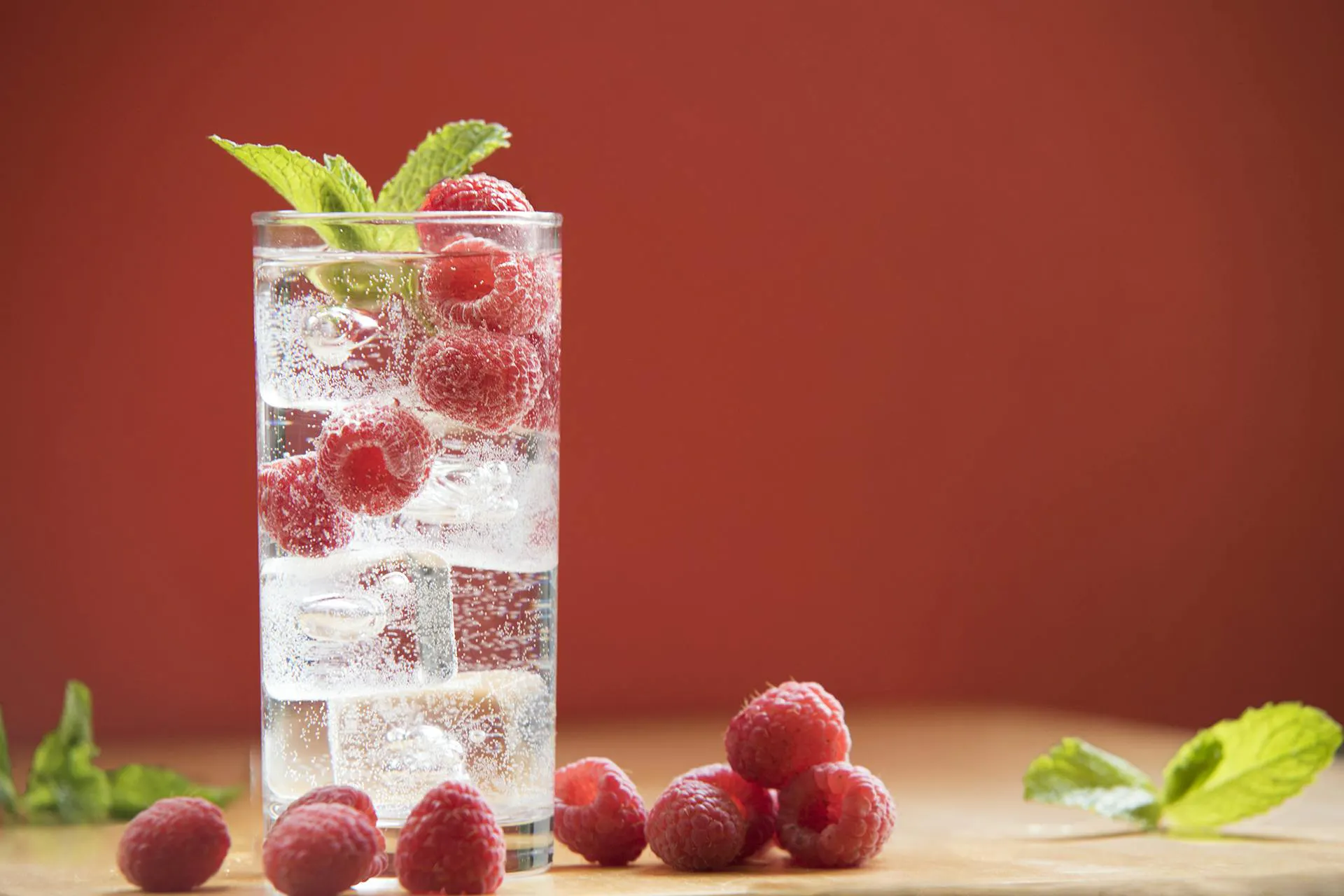 A glass of water with ice and raspberries inside