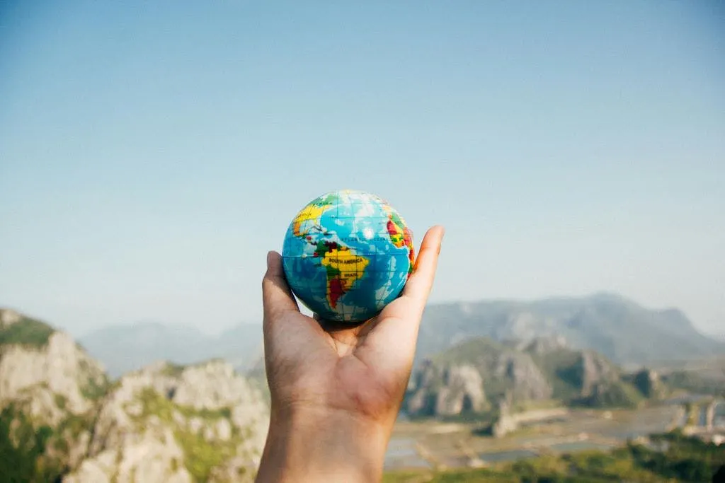 A hand holding up a globe against a backdrop of mountains.