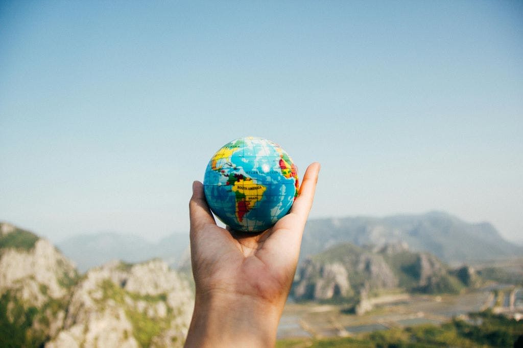 A hand holding up a globe against a backdrop of mountains.