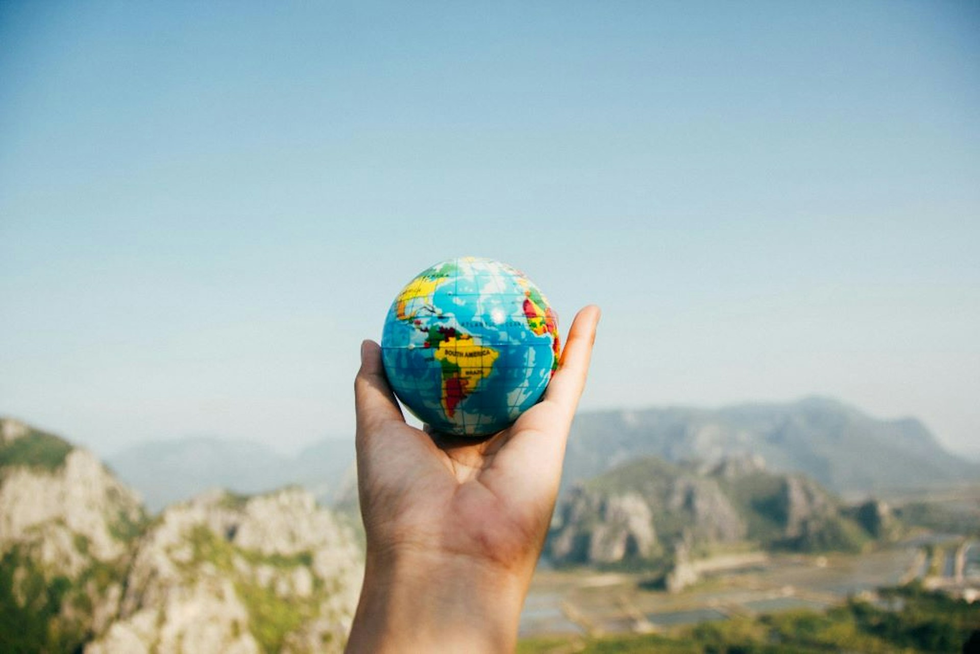 A hand holding up a globe against a backdrop of mountains. 