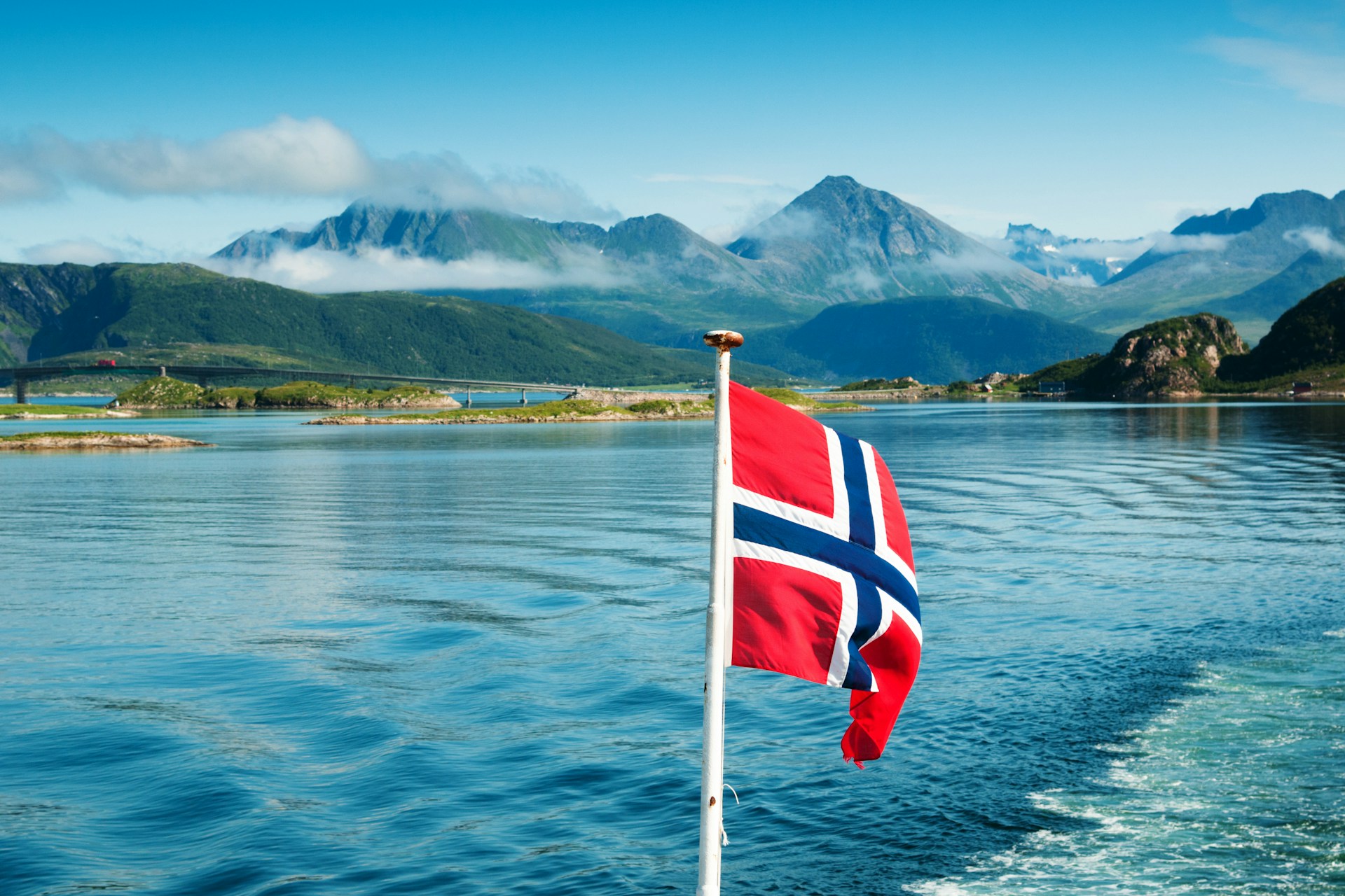 Photo taken from the back of a boat showing the Norwegian flag and a great landscape