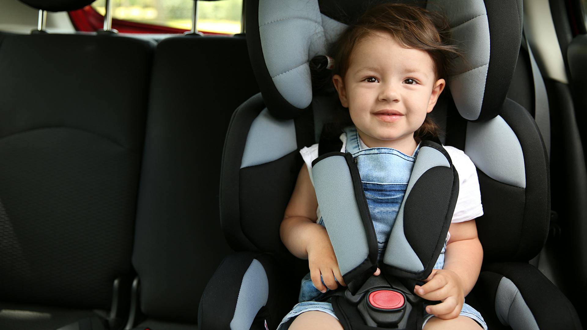 Photo of a little child sitting in the car in a baby seat with the seatbelt on